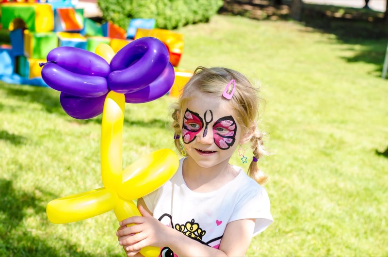 Petite fille maquillée tenant une fleur en ballon sculpté lors d'un anniversaire Anni-Zen