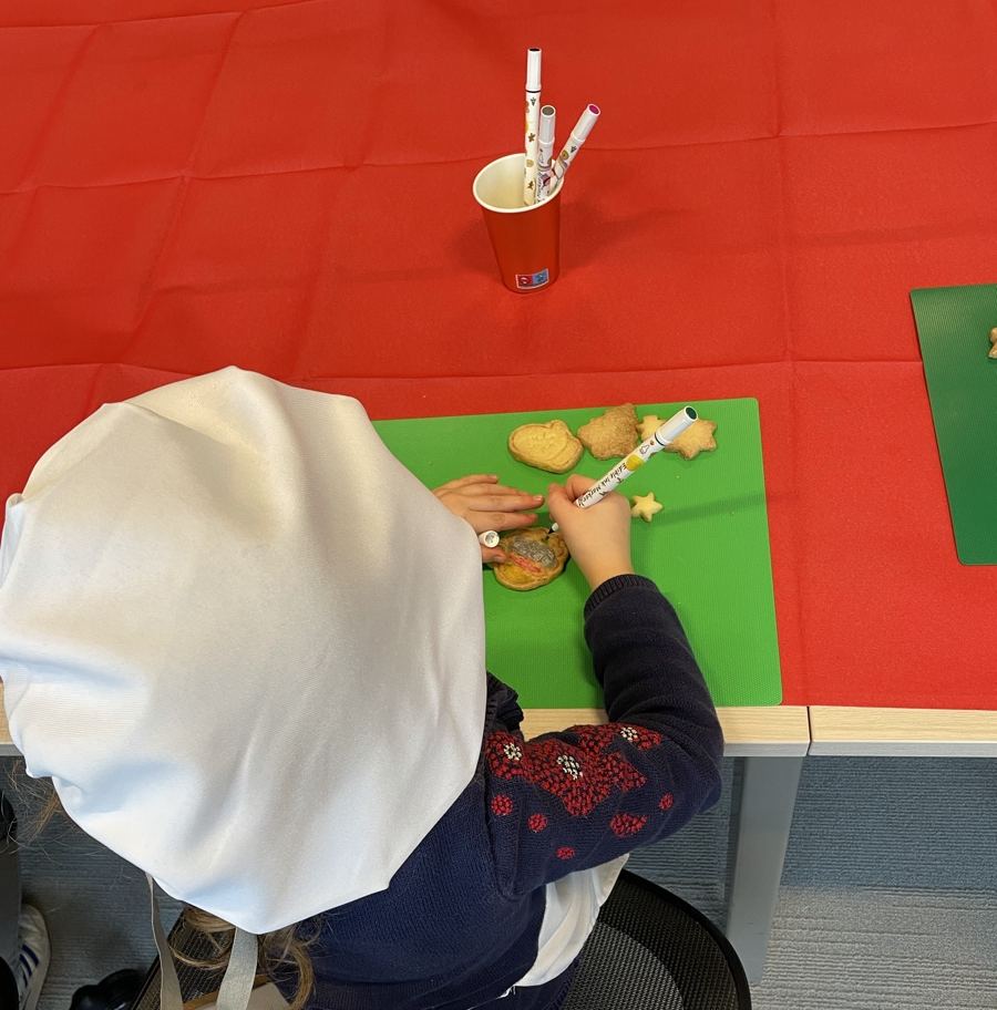 Enfant en toque blanche, vu de dos, décorant des sablés de Noël au feutre alimentaire