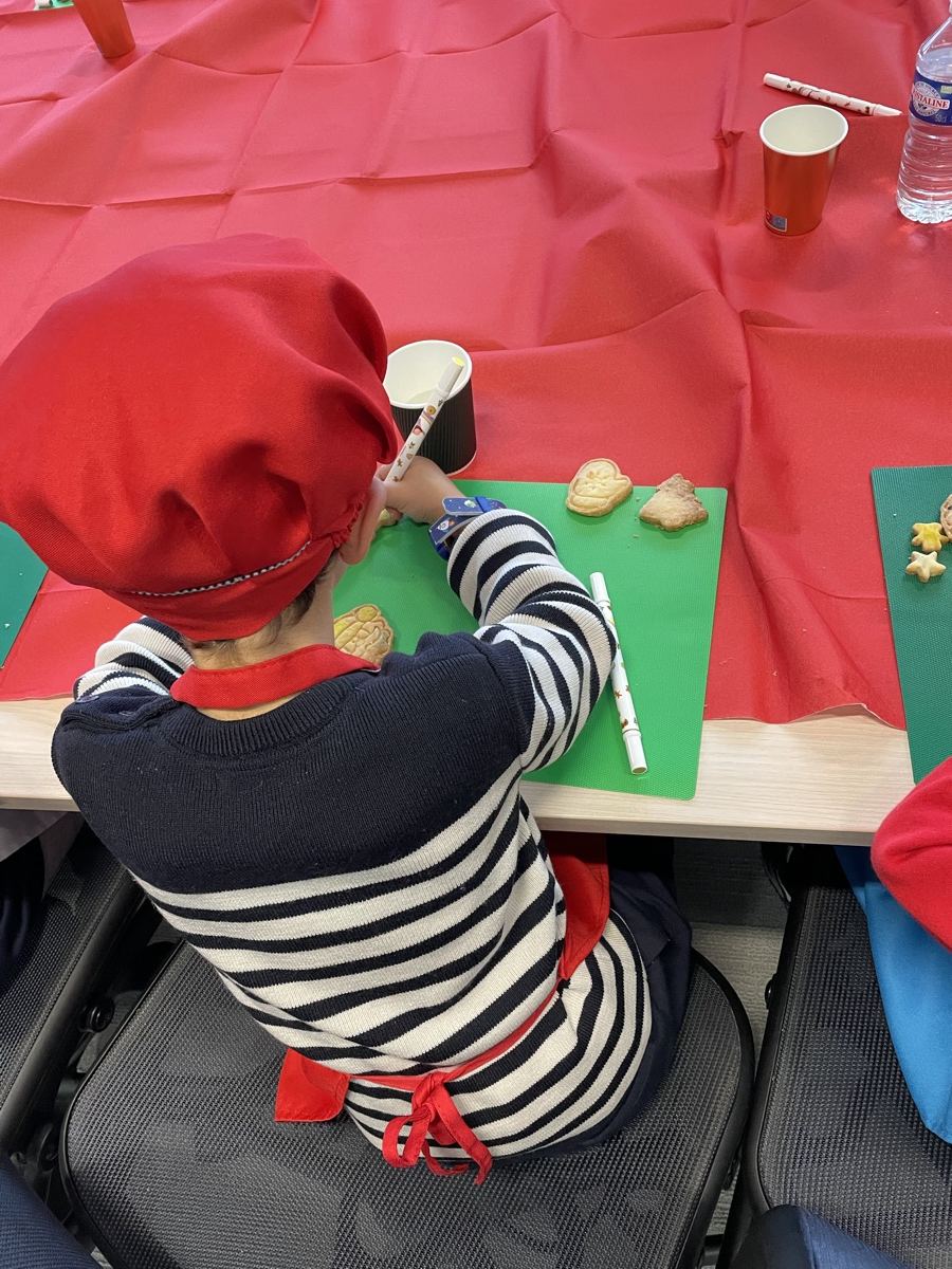 Enfant en toque rouge et marinière, vu de dos, décorant des sablés de Noël